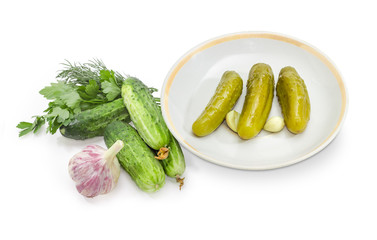 Canned cucumbers on saucer and fresh cucumbers, garlic and greens