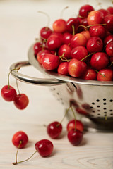 Cherries in a colander on a light wooden background.
