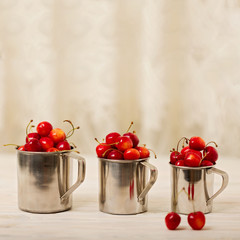 Cherries in metal mugs on a light wooden background.