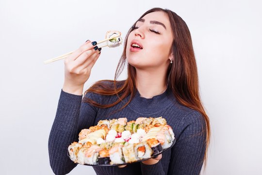 Japanese food, restaurant concept. Young beautiful woman enjoy eating sushi, studio shoot on white background with copy space.