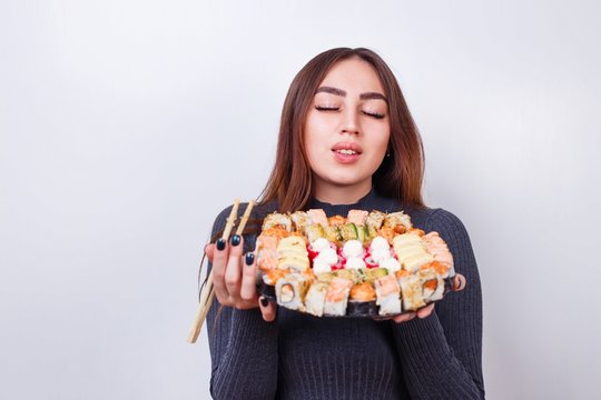 Young pleased beautiful woman with a big sushi rolls set, studio shoot on white background with copy space. Japanese food