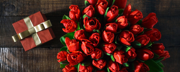 Bouquet red tulips with gift on wooden table copy space