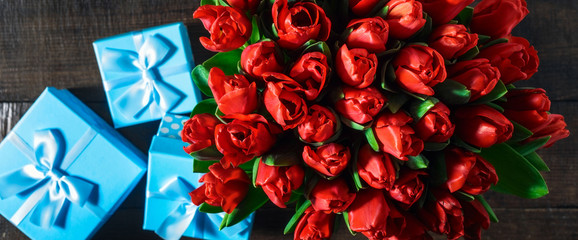 Bouquet of red tulips with gift on dark wooden table