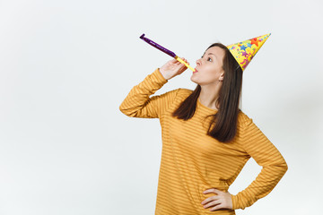 Beautiful caucasian fun young happy woman in yellow clothes and birthday party hat with brown long hair, playing pipe, celebrating and enjoying holiday on white background isolated for advertisement.