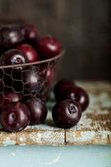 Ripe plums in a basket on a wooden background. Macro photo.