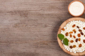 Cottage cheese in bowl with sour cream and raisins on old wooden background with copy space for your text. Top view