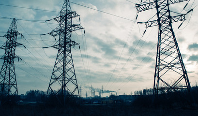 Three electrical pylons and smoking chimneys in the distance.
