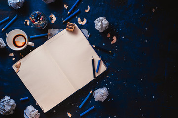 Open notepad with blank pages, crumpled paper balls, pencils, notepads and empty coffee cups on a...