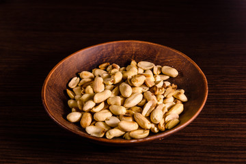 Peeled roasted peanuts in ceramic dish on wooden table