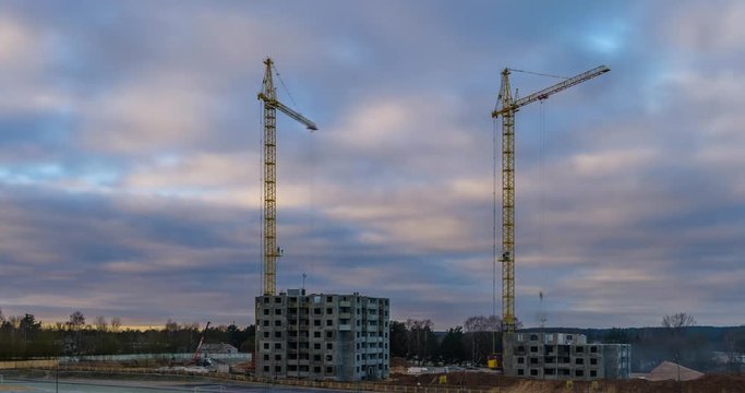 Time lapse of silhouettes of cranes working on a construction site of a multi-storey building in a fast cloudy morning with moon