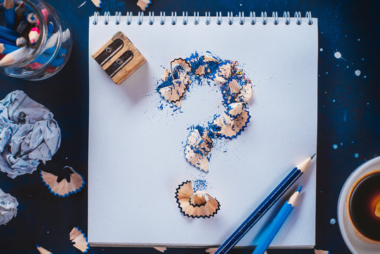 Question mark from pencil shavings with crumpled paper balls, pencils, notepads and empty coffee cups. Still life with writer workplace. Creative block concept.