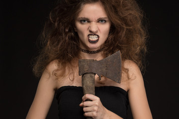 Beautiful girl with a make-up as a witch smiles and holds an ax on a black background for the holiday of Halloween