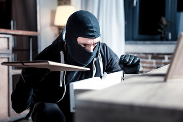 Crime. Dark-eyed skilful masked burglar wearing a uniform and holding a folder while committing a crime