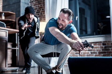 Taking a pistol. Intimidated shocked bearded man sitting with his hands tied and taking a gun while...