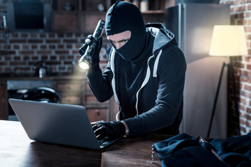 Cyber attack. Determined professional masked hacker sitting at the table and holding a torch and...