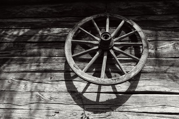 Fototapeta na wymiar Old wooden wheel on the wall of an antique wooden barn, black and white photo
