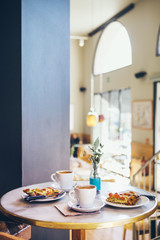 Breakfast for two persons in a cafe, warm quiche and coffee, no people.