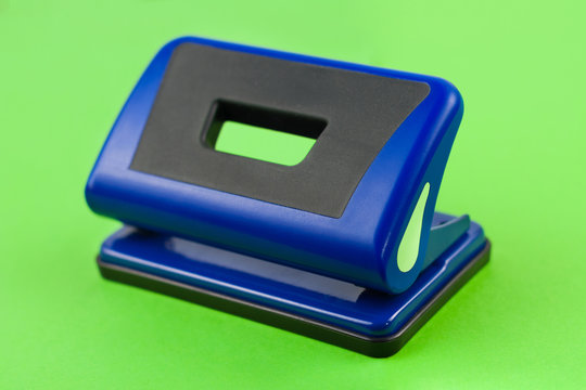 Single blue metal mechanical hole puncher on blank green paper