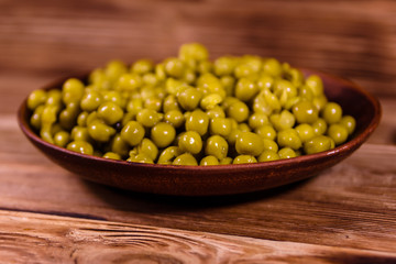 Ceramic plate with canned green pea on wooden table