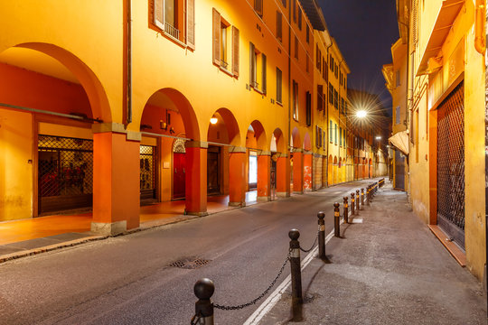 Medieval street portico with bright colored houses in the Old Town at night, Bologna, Emilia-Romagna, Italy