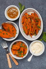 Different types of baked sweet potato with curry and a creamy garlic sauce. White dishes, dark background, top view. Healthy vegan food concept.