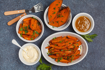 Different types of baked sweet potato with curry and a creamy garlic sauce. White utensils, dark background, top view. Healthy vegan food concept.
