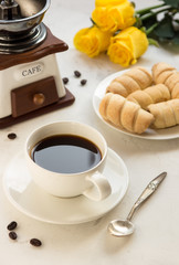 Coffee, sweet bakery and manual coffee grinder on a white table, yellow roses on a background