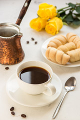 Coffee, jezva and sweet bakery on a white table, yellow roses on a background