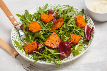 Salad of baked sweet potato with arugula. White plate, light background, top view. Healthy vegan food concept.