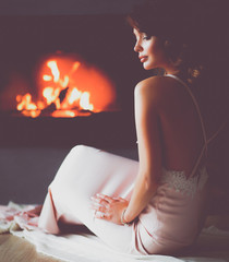Beautiful woman sitting by the fireplace . Classic interior. Beauty, fashion