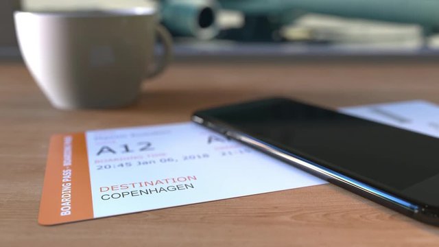 Boarding pass to Copenhagen and smartphone on the table in airport. Travelling to Denmark conceptual animation