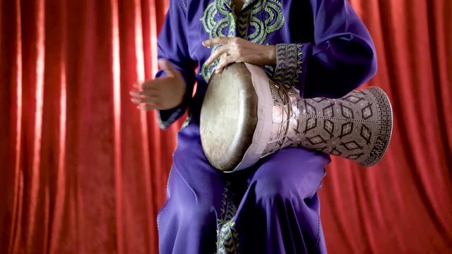A female Arabic percussionist playing the rhythm beladi on a decorated clay doumbek with fish skin head.