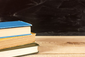 Stack of books on a wooden desk with a blackboard in the background