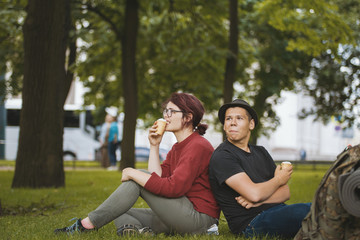 Naklejka premium Couple of teenagers tourists with backpacks eating ice cream and have rest in the city park