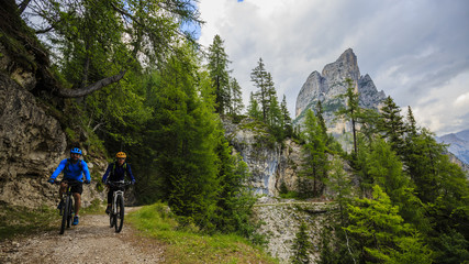 Fototapeta na wymiar Tourist cycling in Cortina d'Ampezzo, stunning rocky mountains on the background. Family riding MTB enduro flow trail. South Tyrol province of Italy, Dolomites.