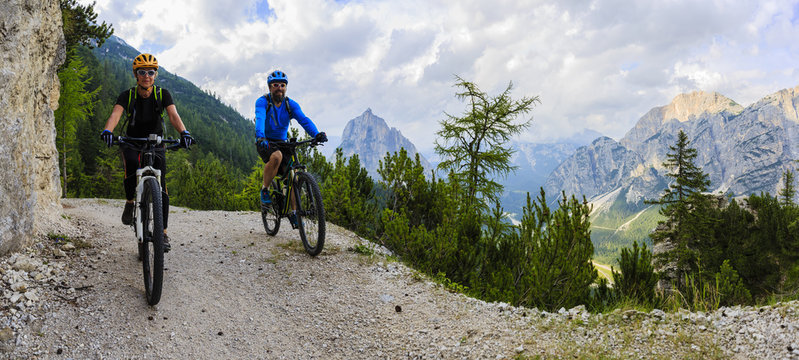 Tourist cycling in Cortina d'Ampezzo, stunning rocky mountains on the background. Family riding MTB enduro flow trail. South Tyrol province of Italy, Dolomites.