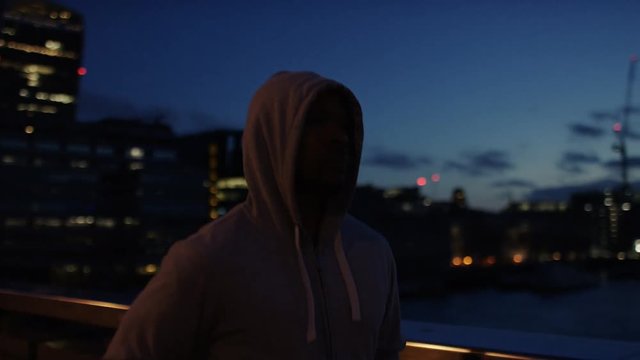 Hooded male athlete jogging in the city early morning, in slow motion 