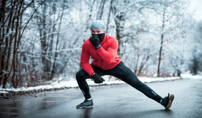 Naklejka premium Winter running exercise, runner stretching on road in snowy forest