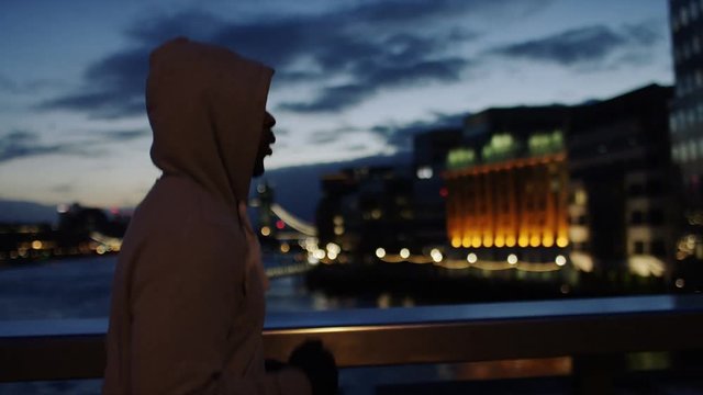Profile steadicam shot of a hooded male athlete jogging in the city early morning, in slow motion