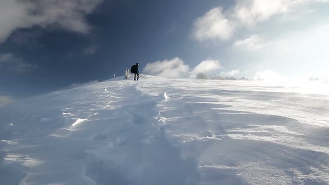 High speed winds drift snow man hiker climber mountaineer standing on mountain ridge during a storm blizzard in winter