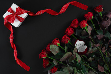 Red roses, ring and gift box on black background