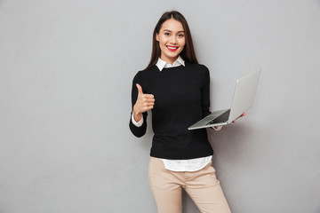 Pleased asian woman in business clothes holding laptop computer