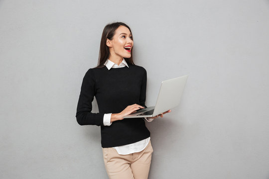 Laughing asian woman in business clothes using laptop computer