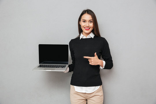 Pleased woman in business clothes showing blank laptop computer screen