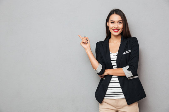 Smiling asian business woman pointing up and looking at camera