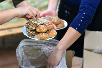 The girl at the table pours the tea into a cup. On the table lie cakes, eclairs. Traditional French dessert. Breakfast in the village. A woman is eating sweets. Against a dark background.