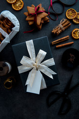 Gift wrapping for Christmas. Top view of table with gift in stylish black paper with white and gold ribbon with tag. Materials and accessories for wrapping gifts. Flat lay.