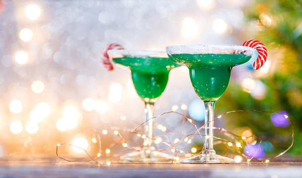 Christmas image of two wine glasses with green cocktail, caramel sticks