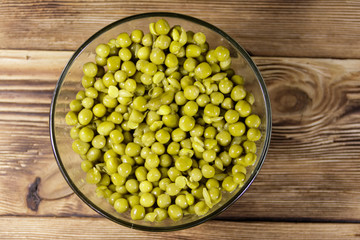 Canned green peas in glass bowl on wooden table