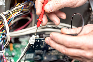 Technician hands with voltmeter above computer motherboard. Repair of computers concept. Toned with...